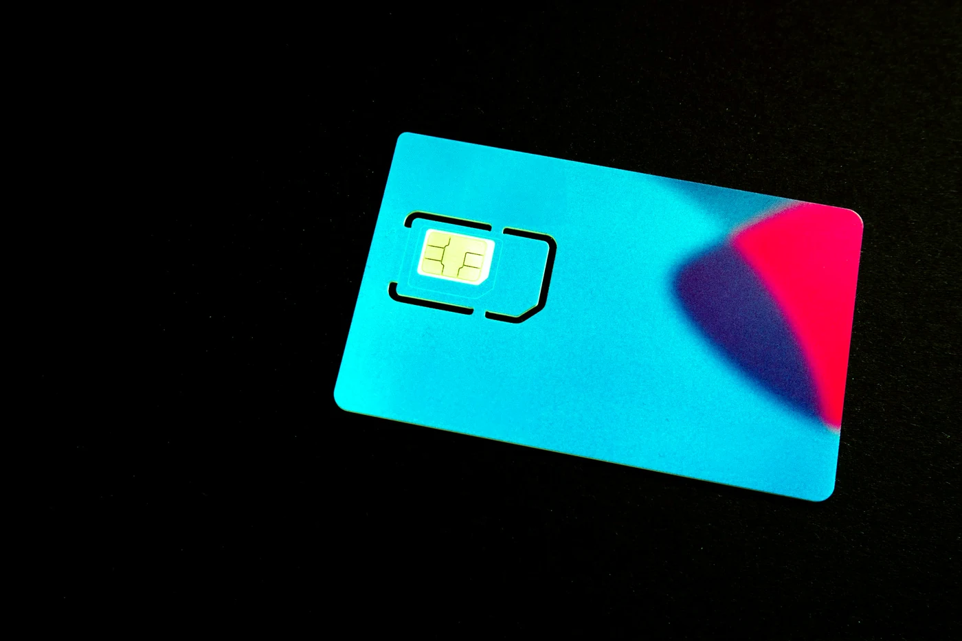 Синяя SIM-карта с золотым чипом лежит на тёмной поверхности